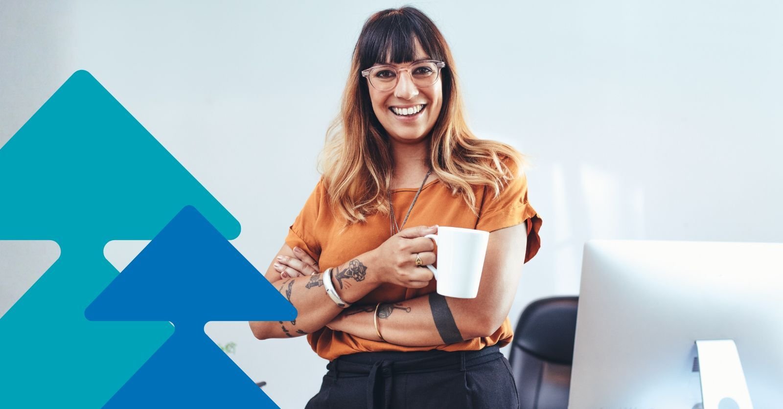 A smiling homecare business owner, standing in front of their desk, holding a mug.