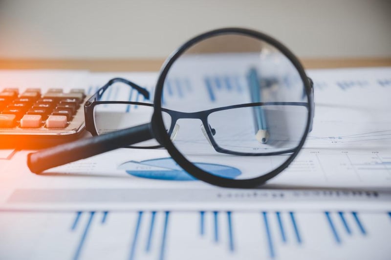 A magnifying glass and a pair of glasses lying on top of printed charts and reports