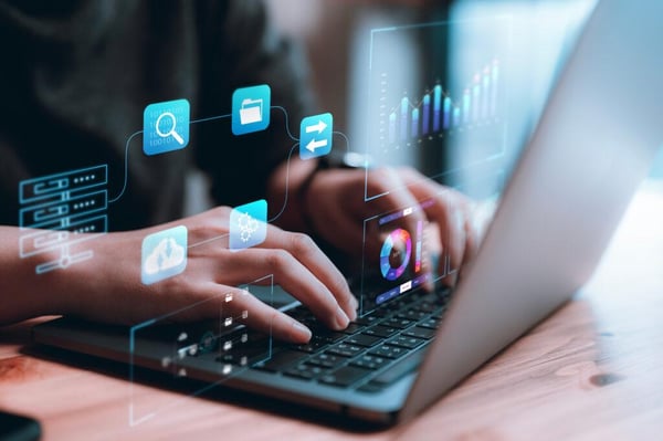 A close-up of hands typing on a laptop with floating graphics indicating technology