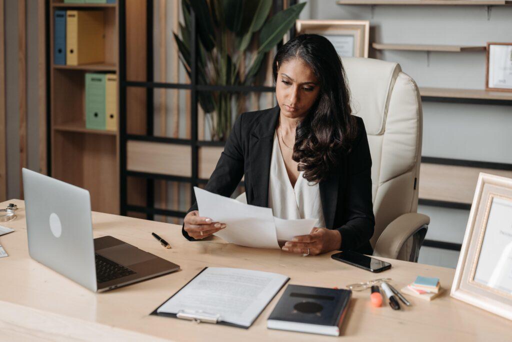A woman in a jacket sitting at a desk looking at some paperwork