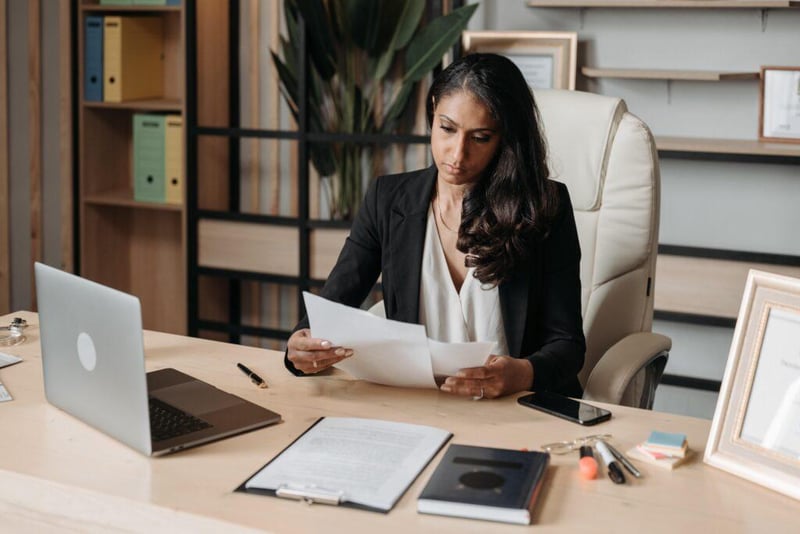 A woman in a jacket sitting at a desk looking at some paperwork