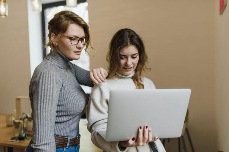 Two women looking at a laptop, one is standing with her hand on the shoulder of the other